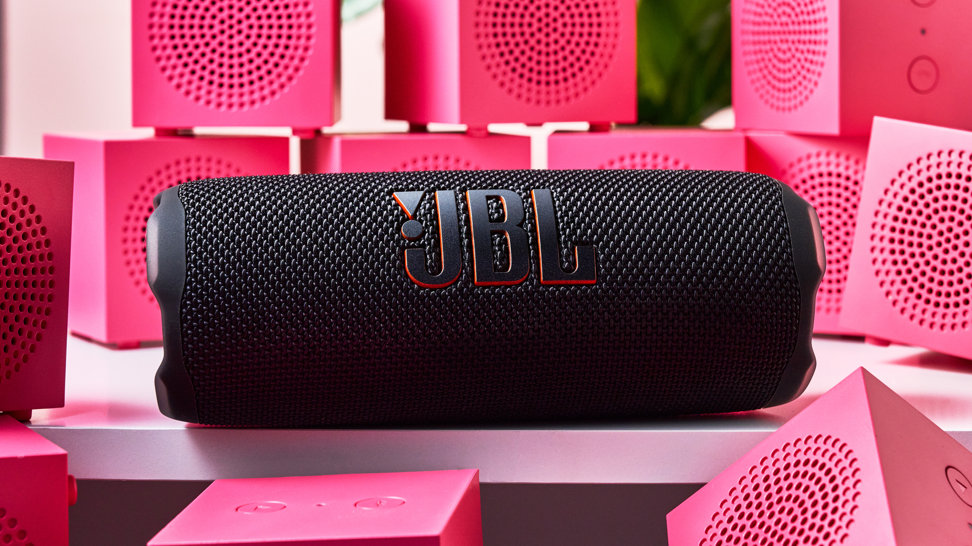 A closeup of the JBL Flip 7 surrounded on all sides by pink IKEA Kallsup speakers.