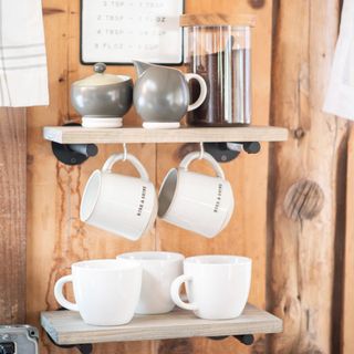 Typo ceramic coffee mugs on shelf and hanging on open shelves against rustic wood cladding