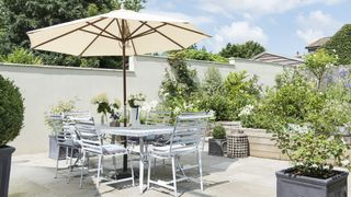 A garden patio in a white colour scheme with table and chairs on a summers day