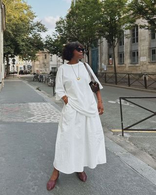 French fashion influencer Frann Fyne wearing a white T-shirt and maxi skirt with ballet flats and a pendant necklace.