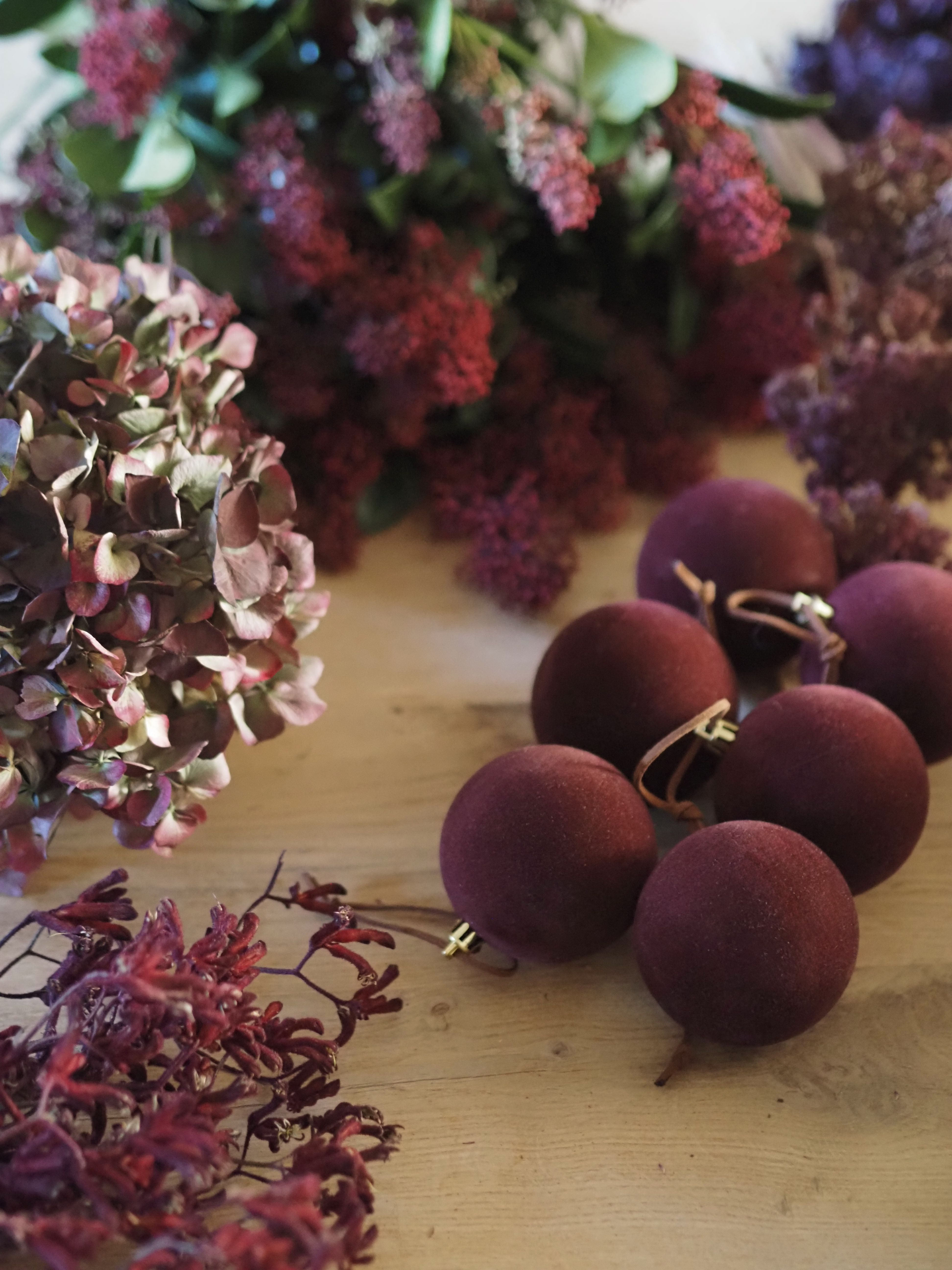 close up of burgundy baubles on a table with burgundy hydrangeas and flowers