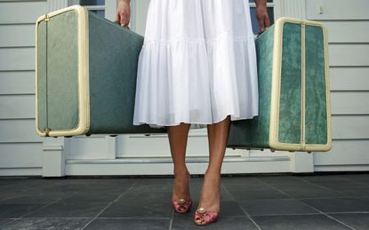 Woman leaving entrance door carrying two suitcases, low section