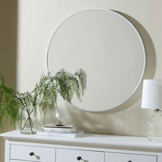 white circular mirror above white chest of drawers