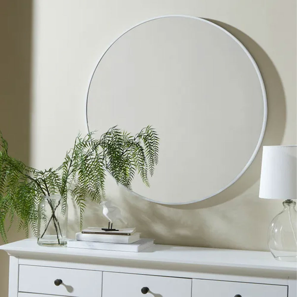 white circular mirror above white chest of drawers