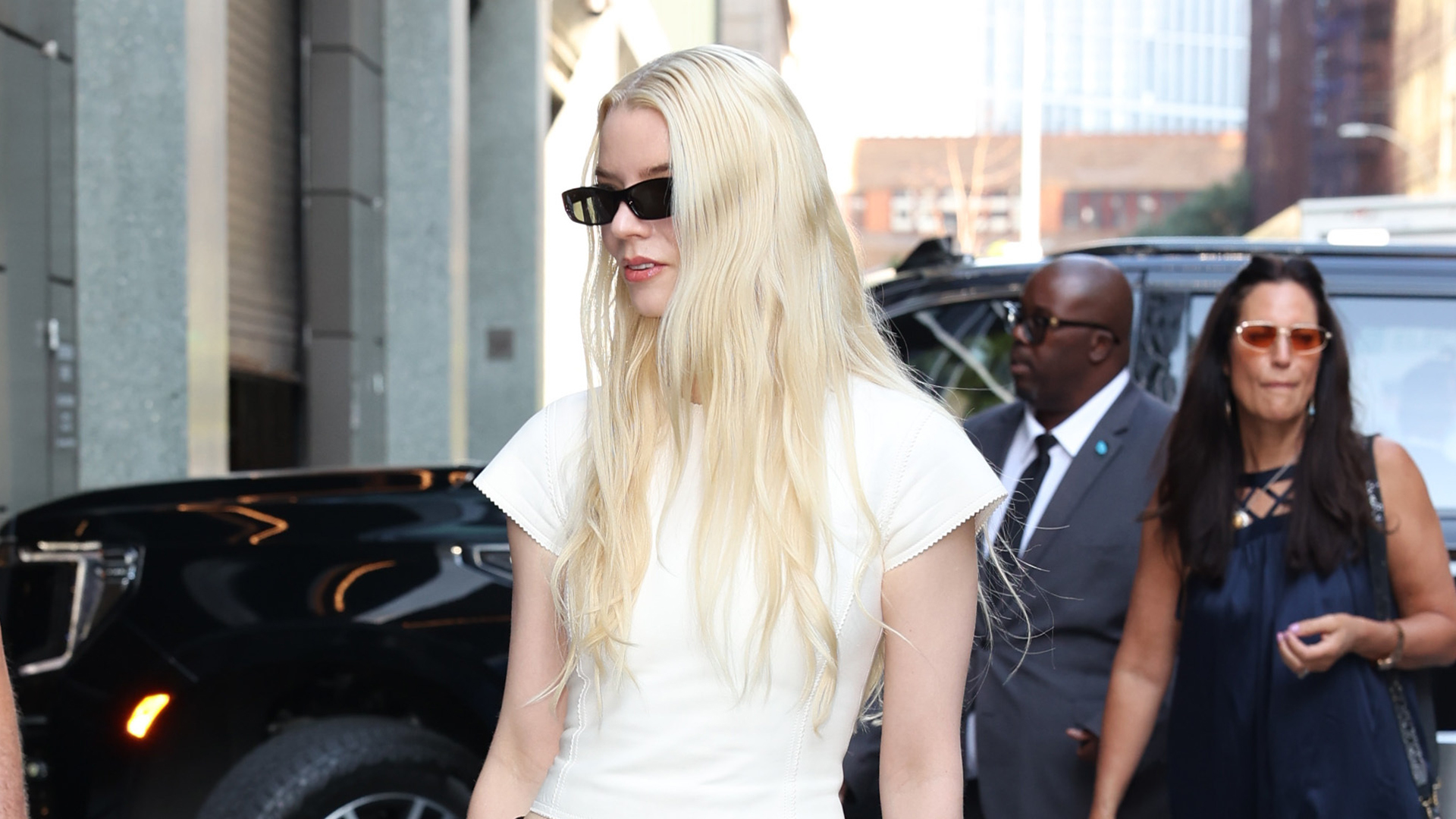 Anya Taylor-Joy wearing a white T-shirt, black low-rise trousers, and black pointed-toe heels 