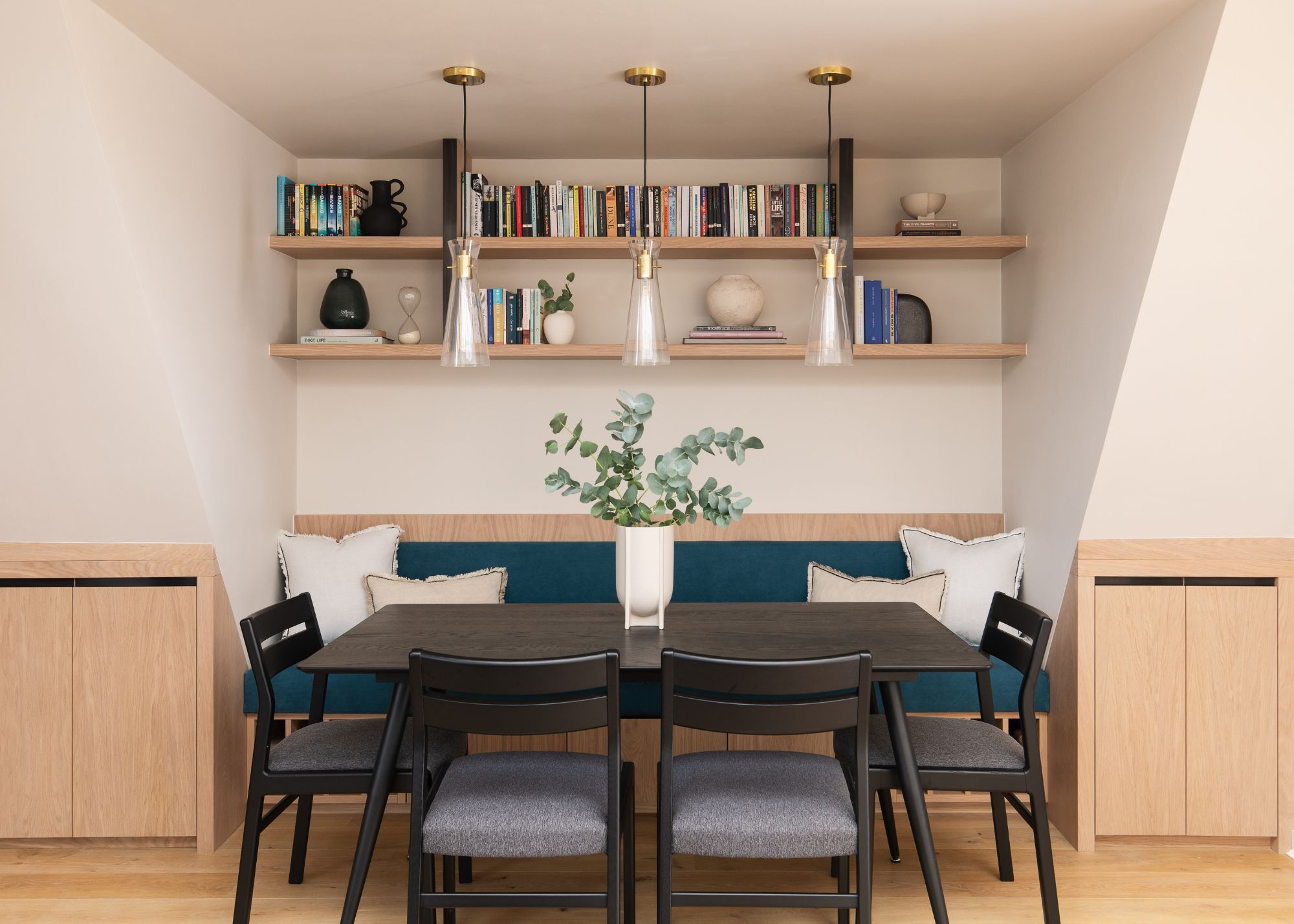 A dining nook built into an alcove with a black dining table and chairs, floating shelves, and banquette seating.
