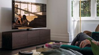 Samsung QN75Q80TAFXZA on TV stand opposite sofa with TV watchers