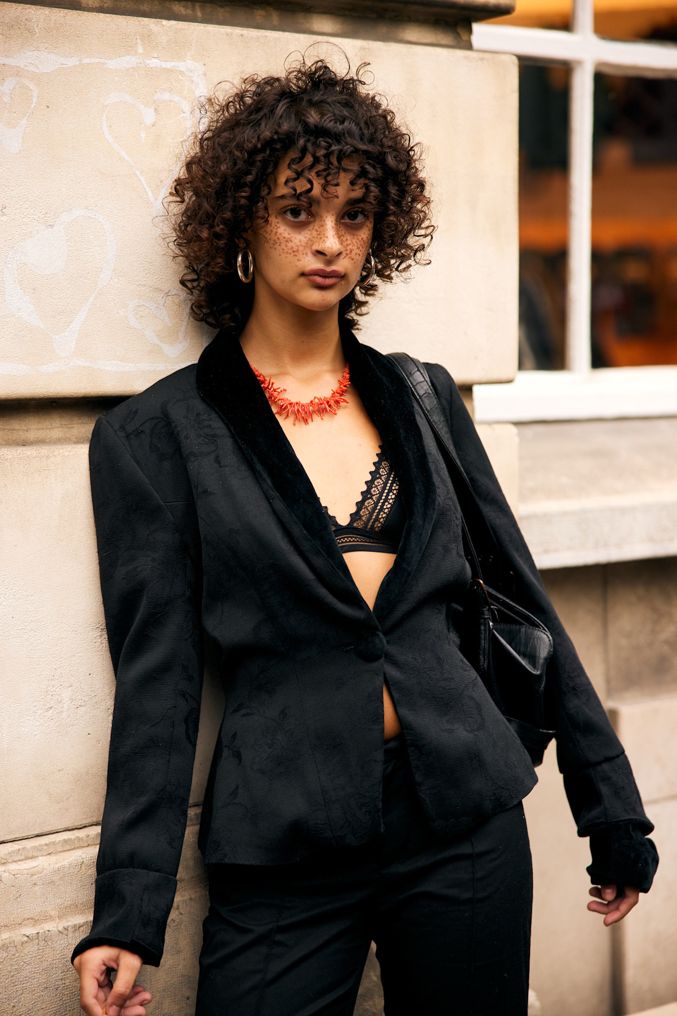 a black woman with curly hair in a black blazer and red necklace
