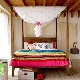 four poster bed with bright coloured linen neutral walls and jute rug