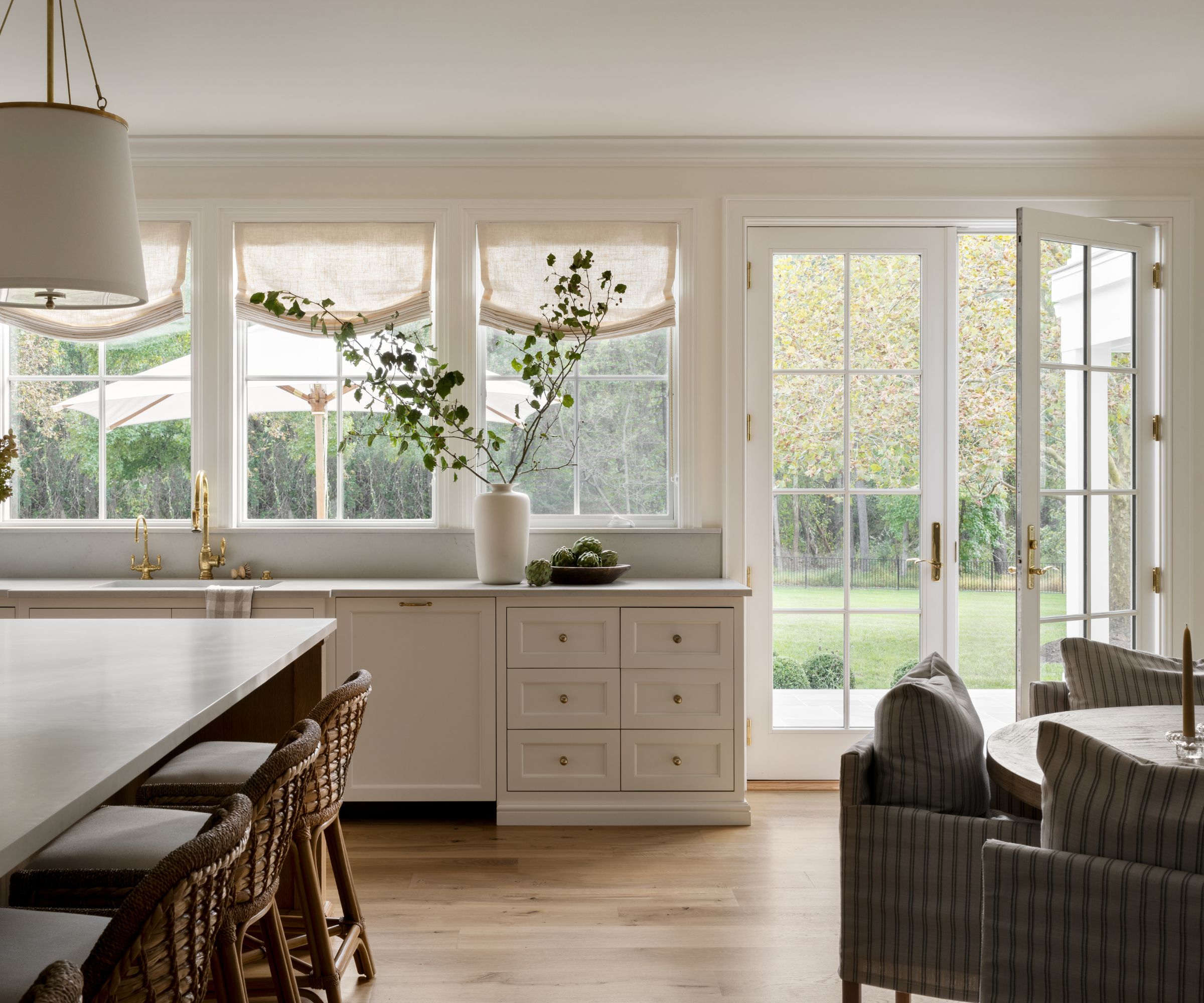 A warm neutral kitchen with off-white cabinets, gray countertops, and large French doors leading to the backyard