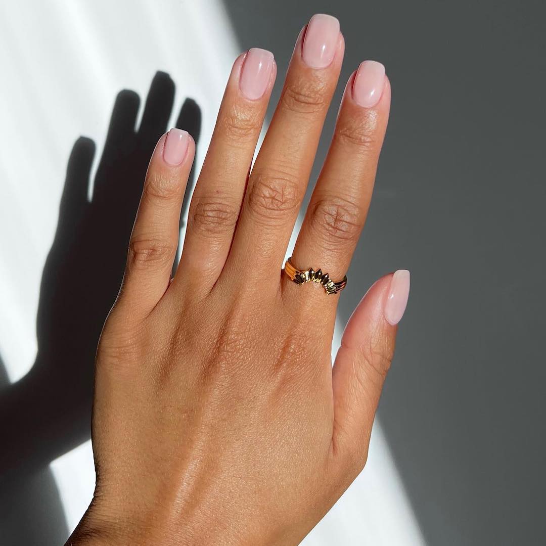 A photo of Iram Shelton's hands with a square manicure with a sheer pink nail colour on top
