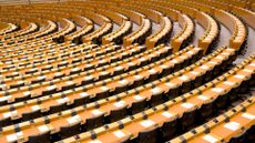 A shot of the empty European parliament, with concentric desks arranged around a central point off camera to the left.