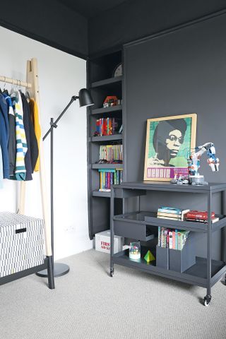 Kid's bedroom with black walls and ceiling, white feature wall, built-in shelving, freestanding clothes rail and black wheeled storage trolley