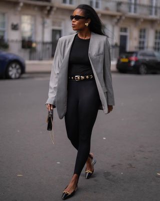 Marilyn Nwawulor-Kazemaks wearing a gray blazer with a black spring outfit and gold details