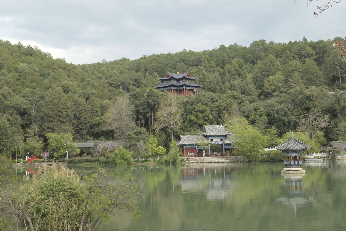 A Chinese temple nestled among trees, with a still lake in the foreground