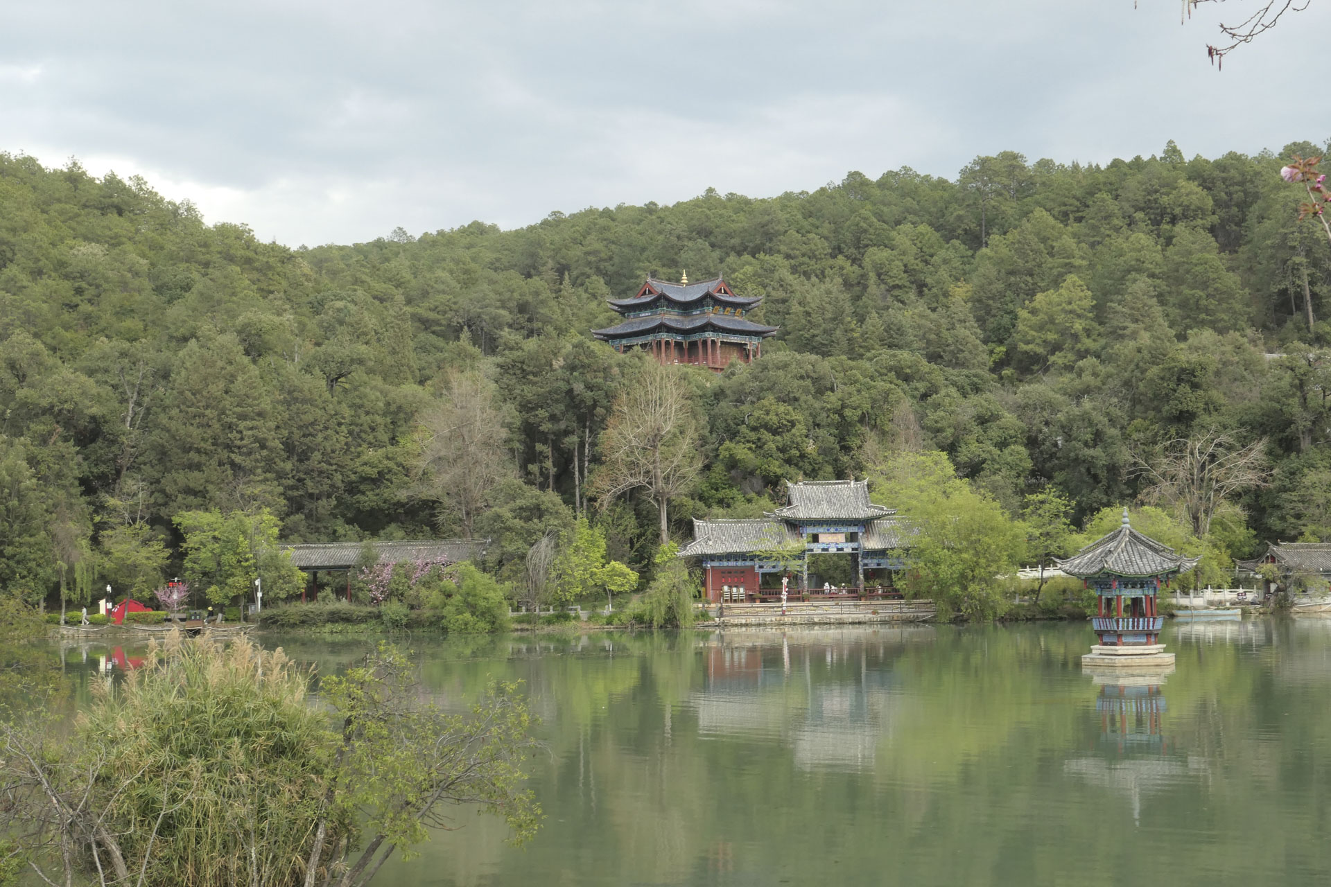 A Chinese temple nestled among trees, with a still lake in the foreground