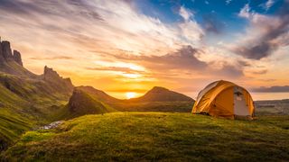 A tent on a hillside with the sun peeking over the horizon in the distance