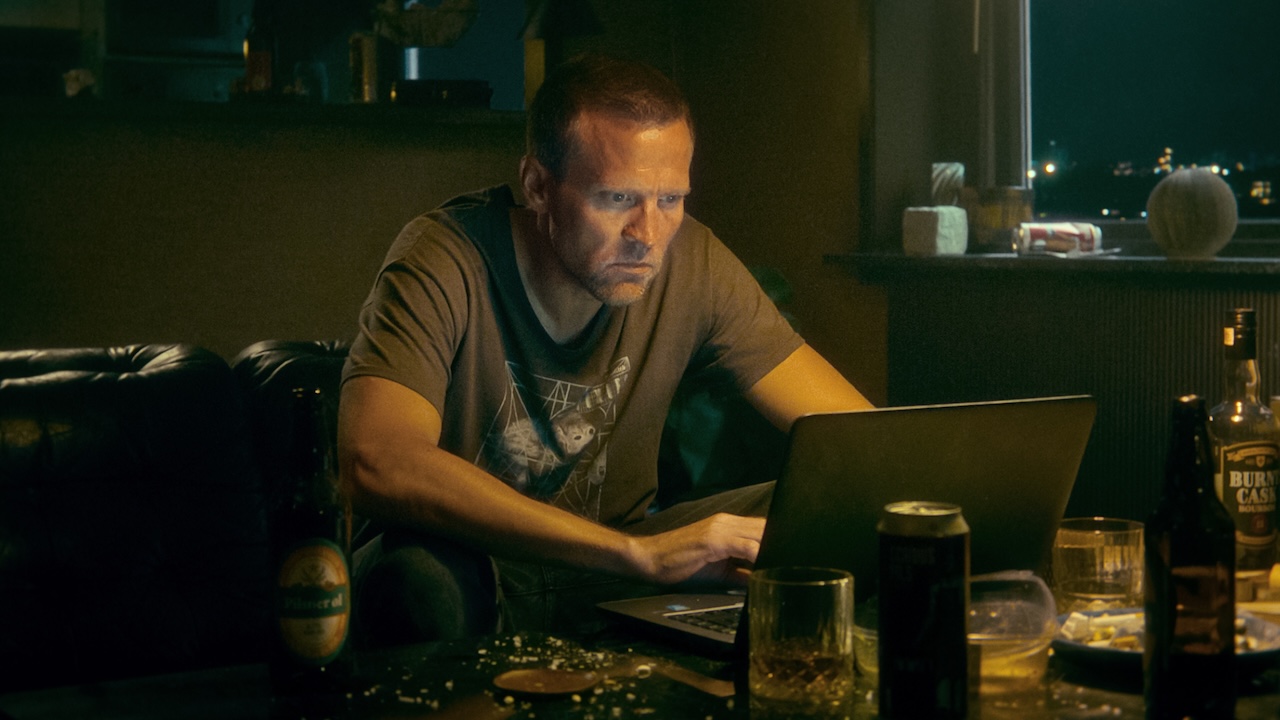 Tobias Santelmann as Harry Hole typing on laptop on messy table in Detective Hole
