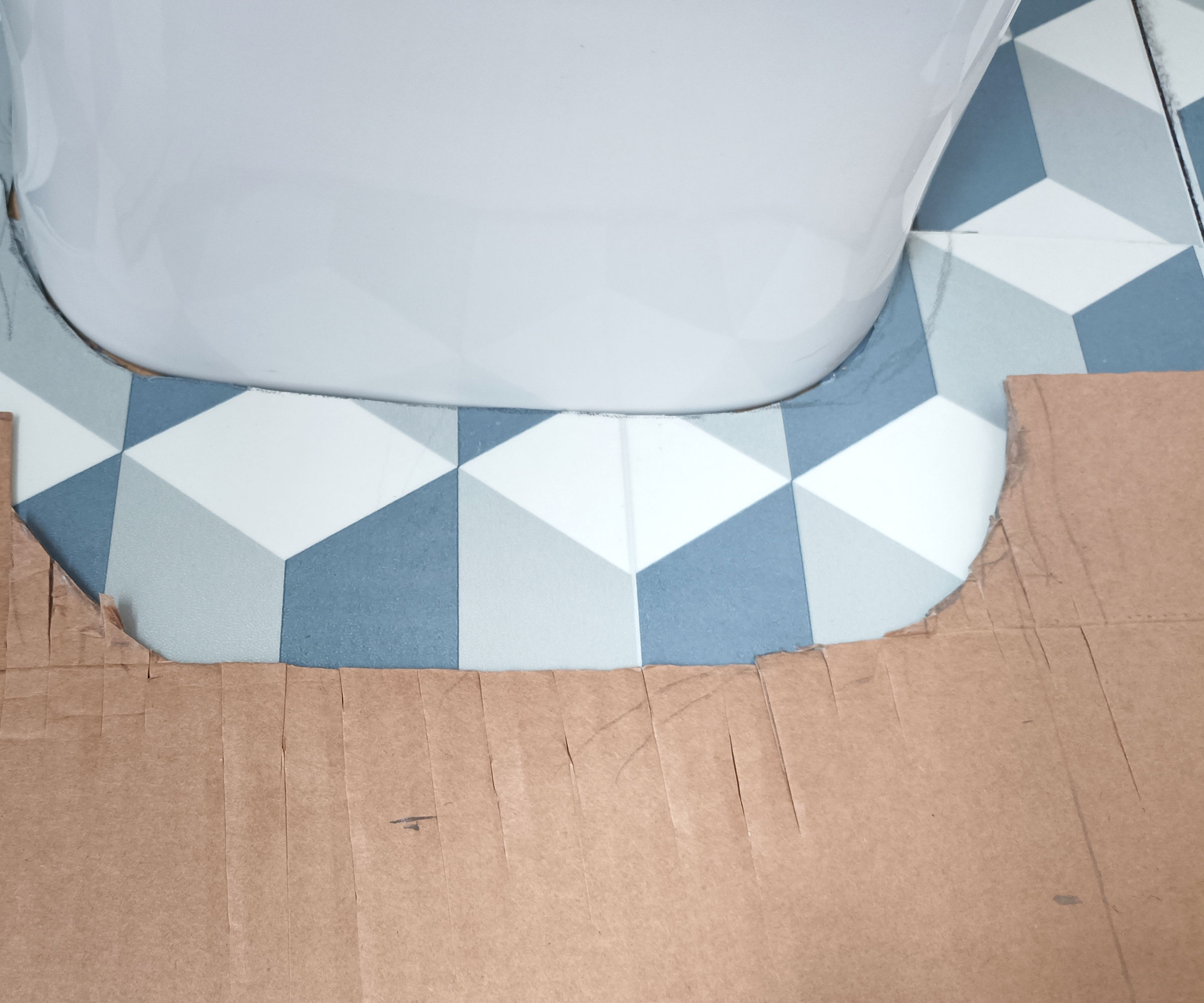 Cut cardboard template with a curve, and cut peel-and-stick tile up against the base of toilet