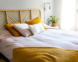 yellow bedding with a nightstand and wall sconce next to it