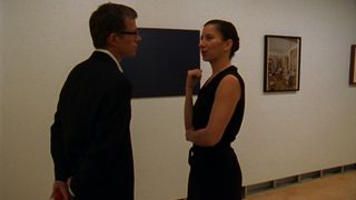 man and woman in black dress talking in a gallery