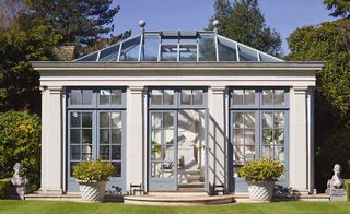 a Haddonstone traditional style orangery made with modern materials – a standalone white and blue orangery with potted plants outside the doors