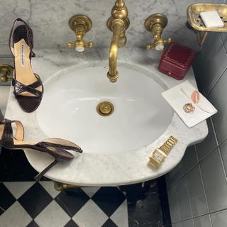 A flat lay on a marble sink featuring Manolo Blahnik heels and a gold Cartier Tank watch.