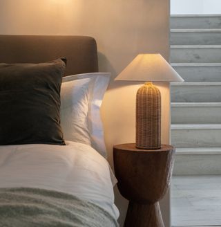 A neutral bedroom with a small bedside table, oblong shaped lamp base with a cream shade