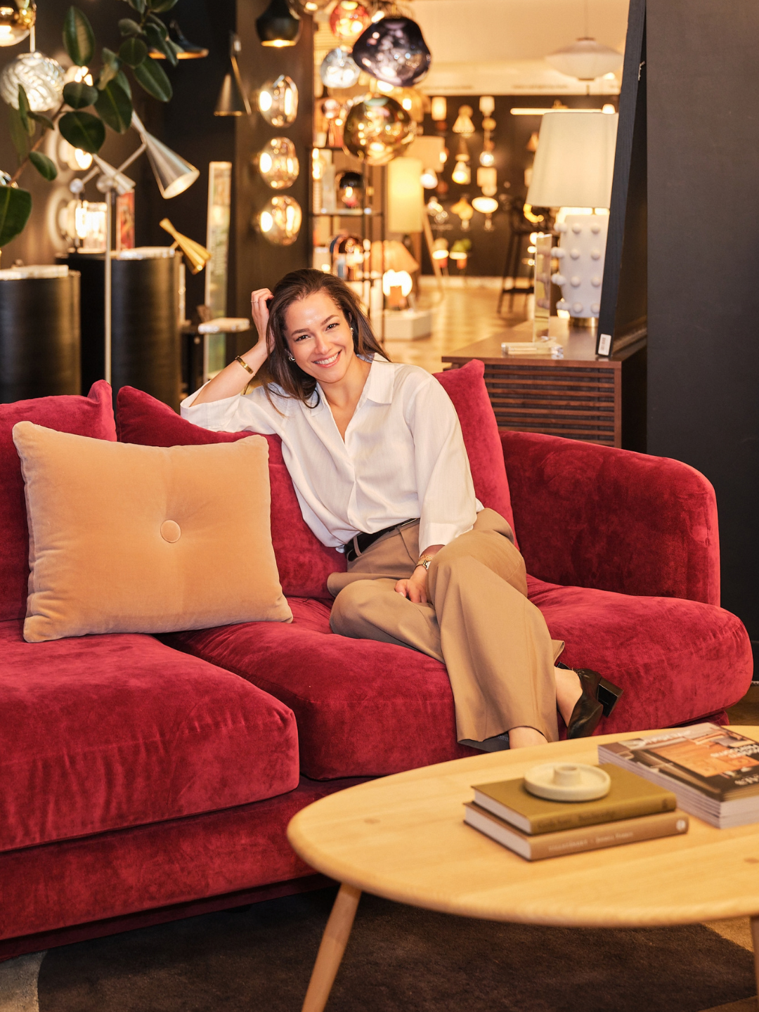 Interior stylist Miaad Latoof sitting on the red velvet Heal&rsquo;s Rafi sofa, showing its generous proportions and relaxed, sink-in comfort.