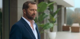 Fred (James Purefoy), wearing a suit and a thoughtful expression, stands in the grounds of a fancy-looking house which is visible but out of focus behind him