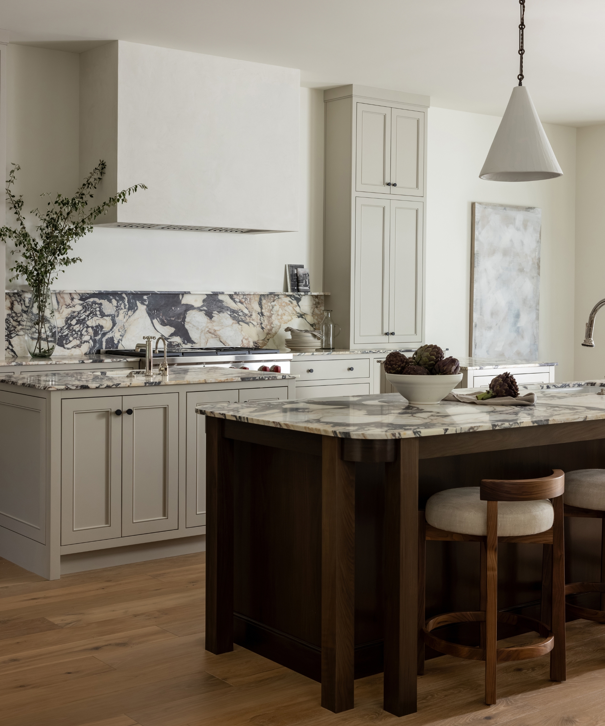 A neutral kitchen with a dark wood island, white walls, marble countertops, and cabinets painted Revere Pewter by Benjamin Moore