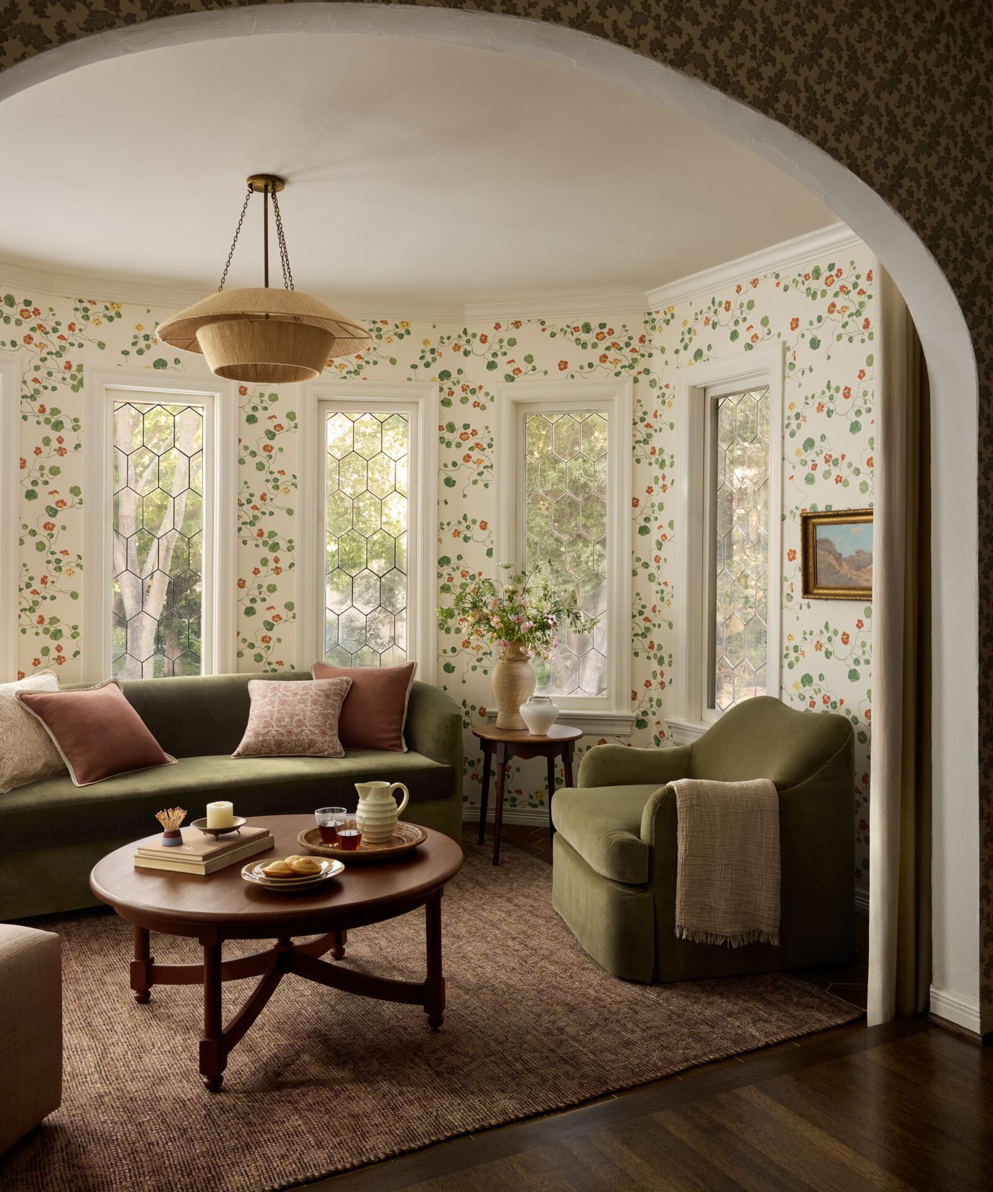 a round living room with green furniture, a wooden coffee table, pillows, and floral speckled wallpaper