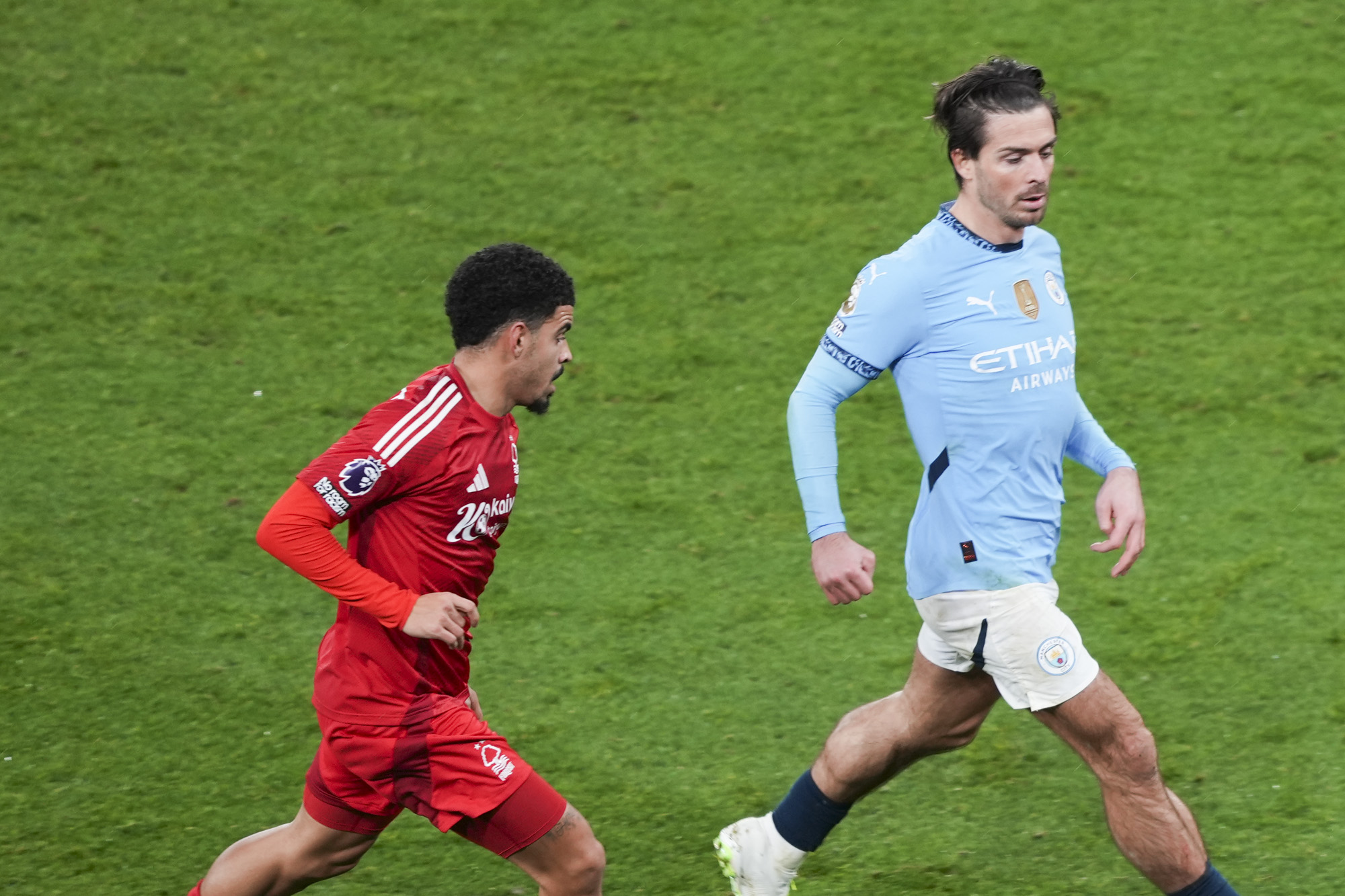 Manchester City player Jack Grealish kicking ball during Premier League match, tracked by Morgan Gibbs-White