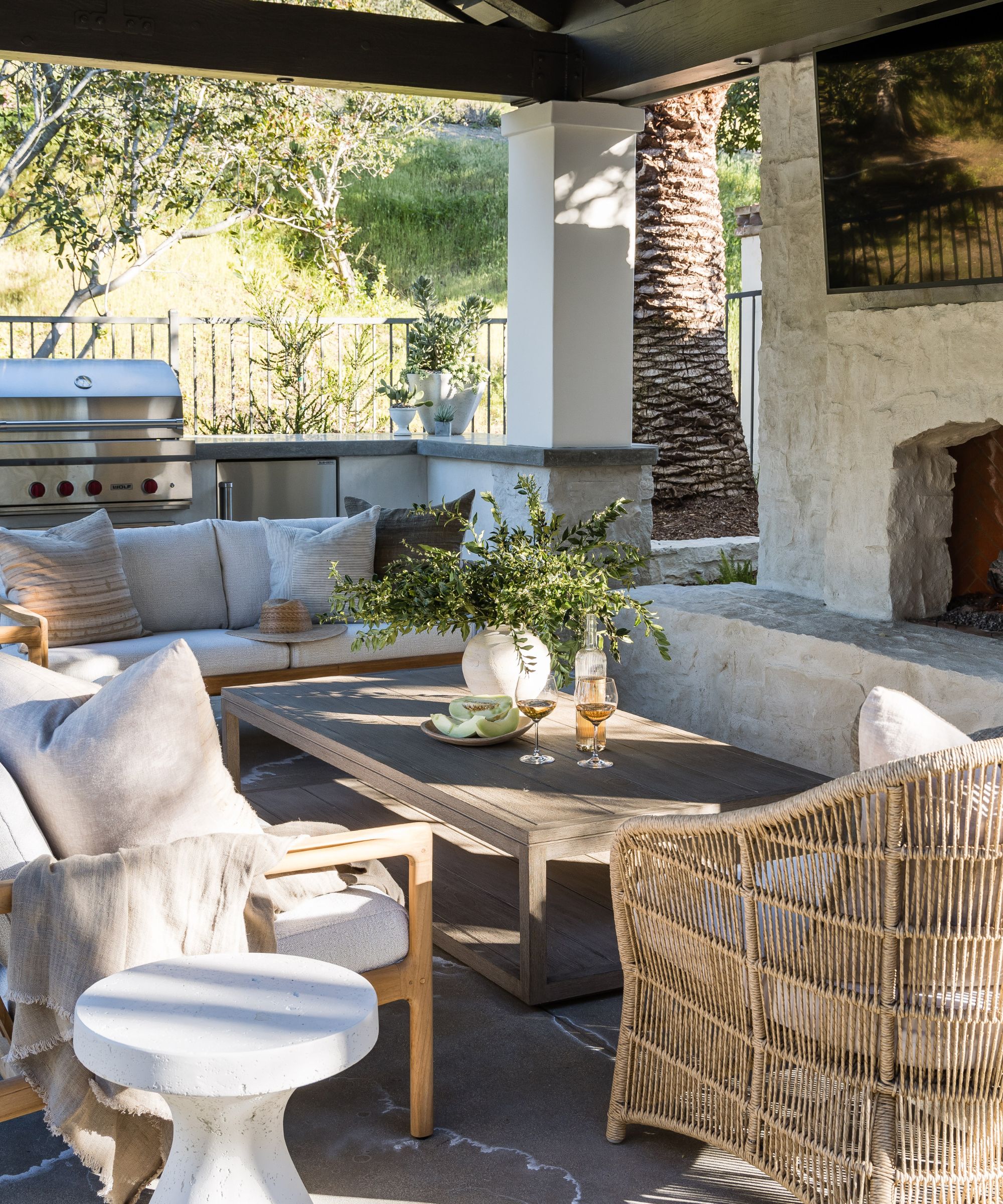 rustic coastal outdoor living room area with a stone fireplace wicker furniture and an outdoor kitchen bar