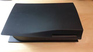 En svart PS5 utan stativ på ett träbord
