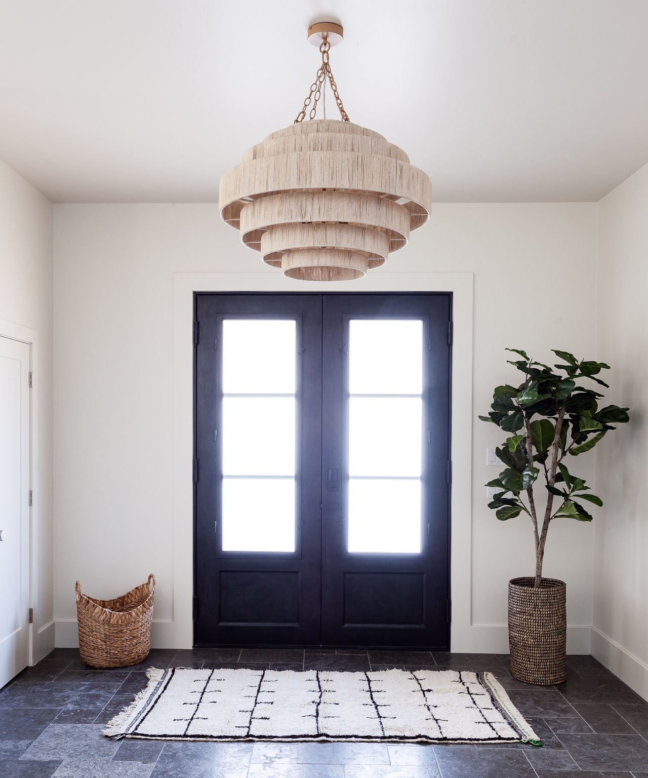 Airy entryway with statement pendant shade, large indoor plant and paneled glass front door