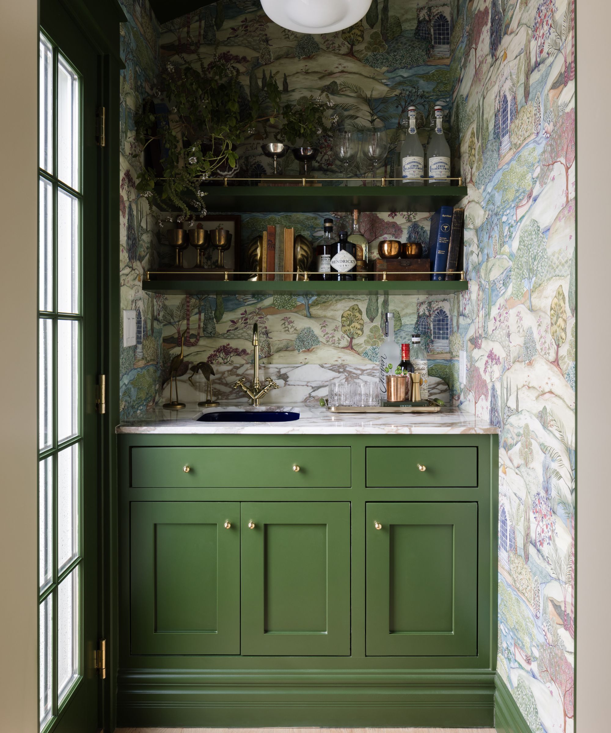 a compact bar with wallpapered walls, glass door, green cabinetry, small blue sink and open shelves