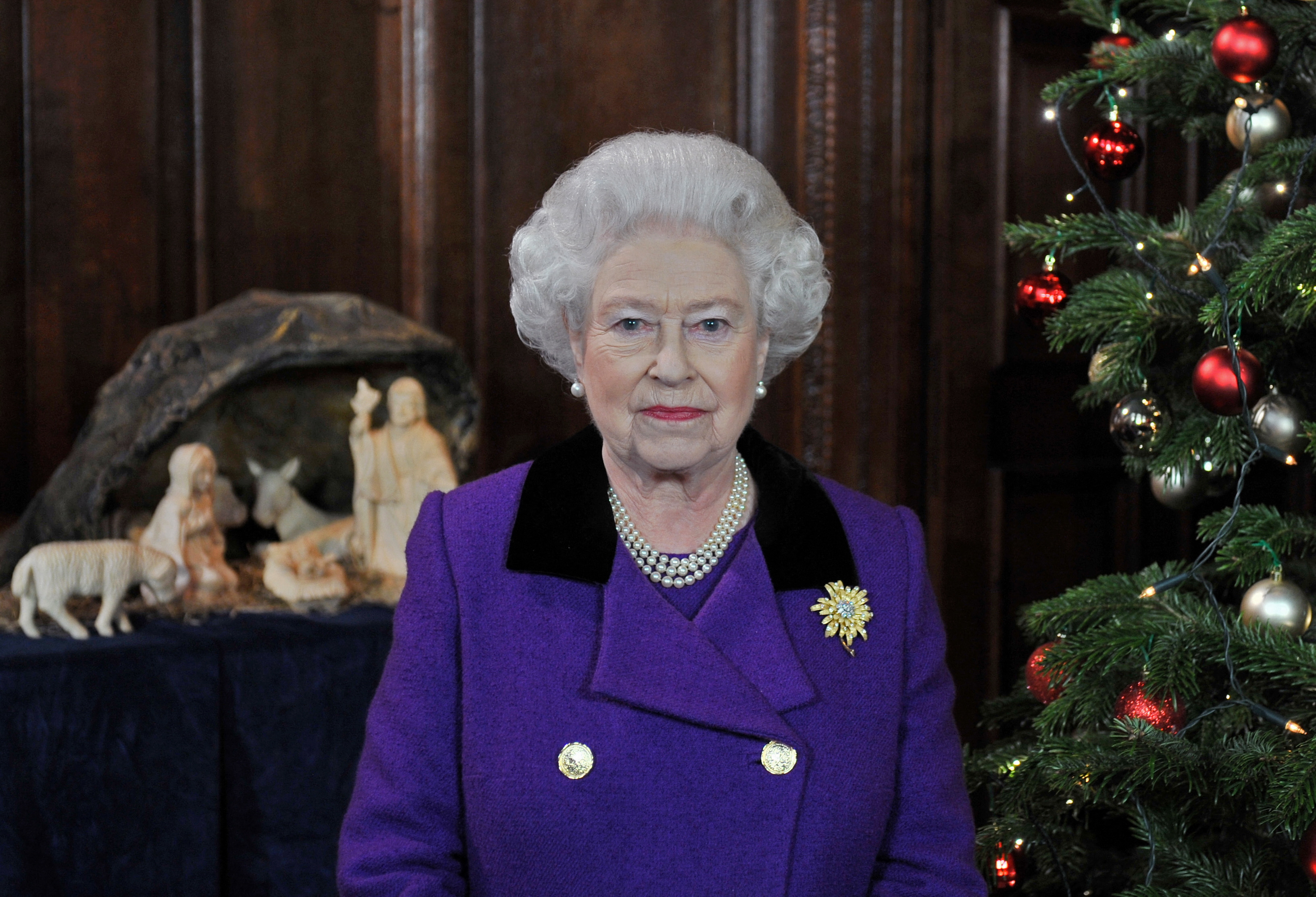 Queen Elizabeth wearing a purple coat standing by a nativity scene