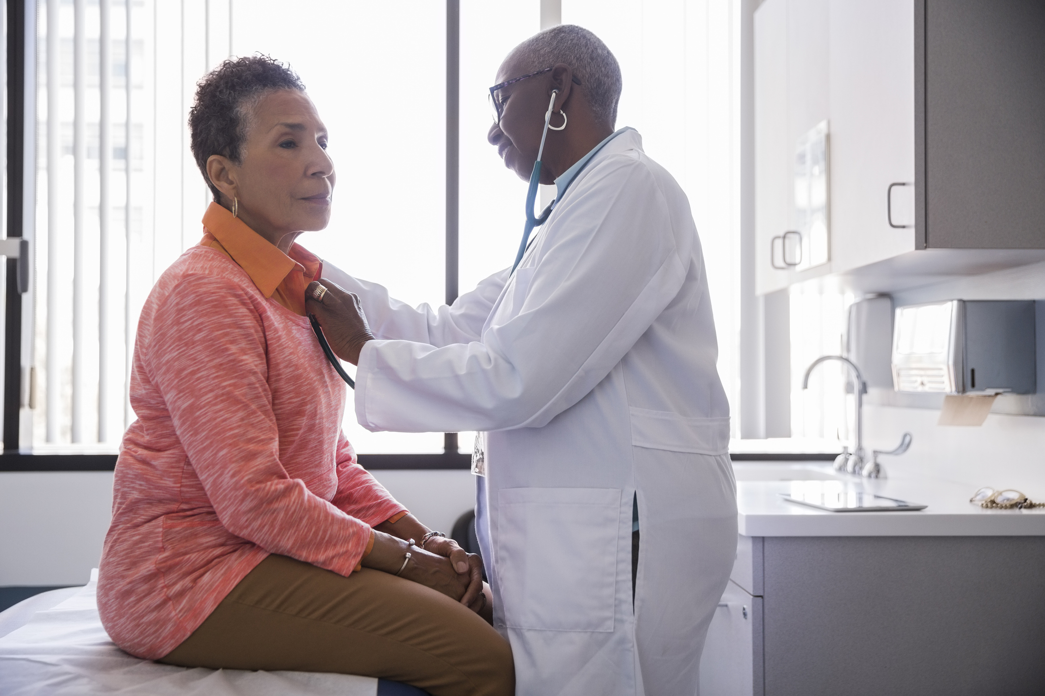 Smiling female doctor examining senior patient in hospital - stock photo