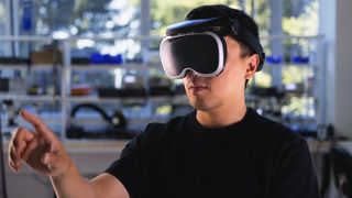 A photo of a man wearing the Meta Boba 3 prototype headset with a finger raised to tap a virtual object.