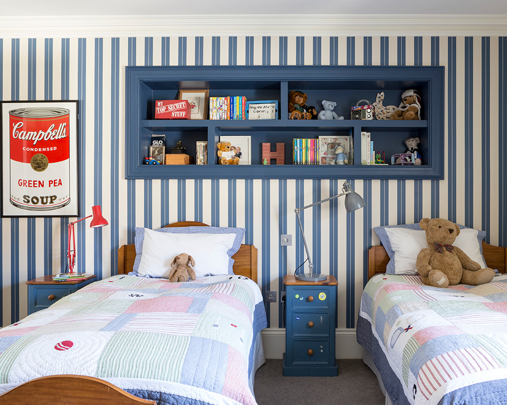 Blue and white striped wallpaper and built-in alcove shelving behind twin beds with patchwork quilts.