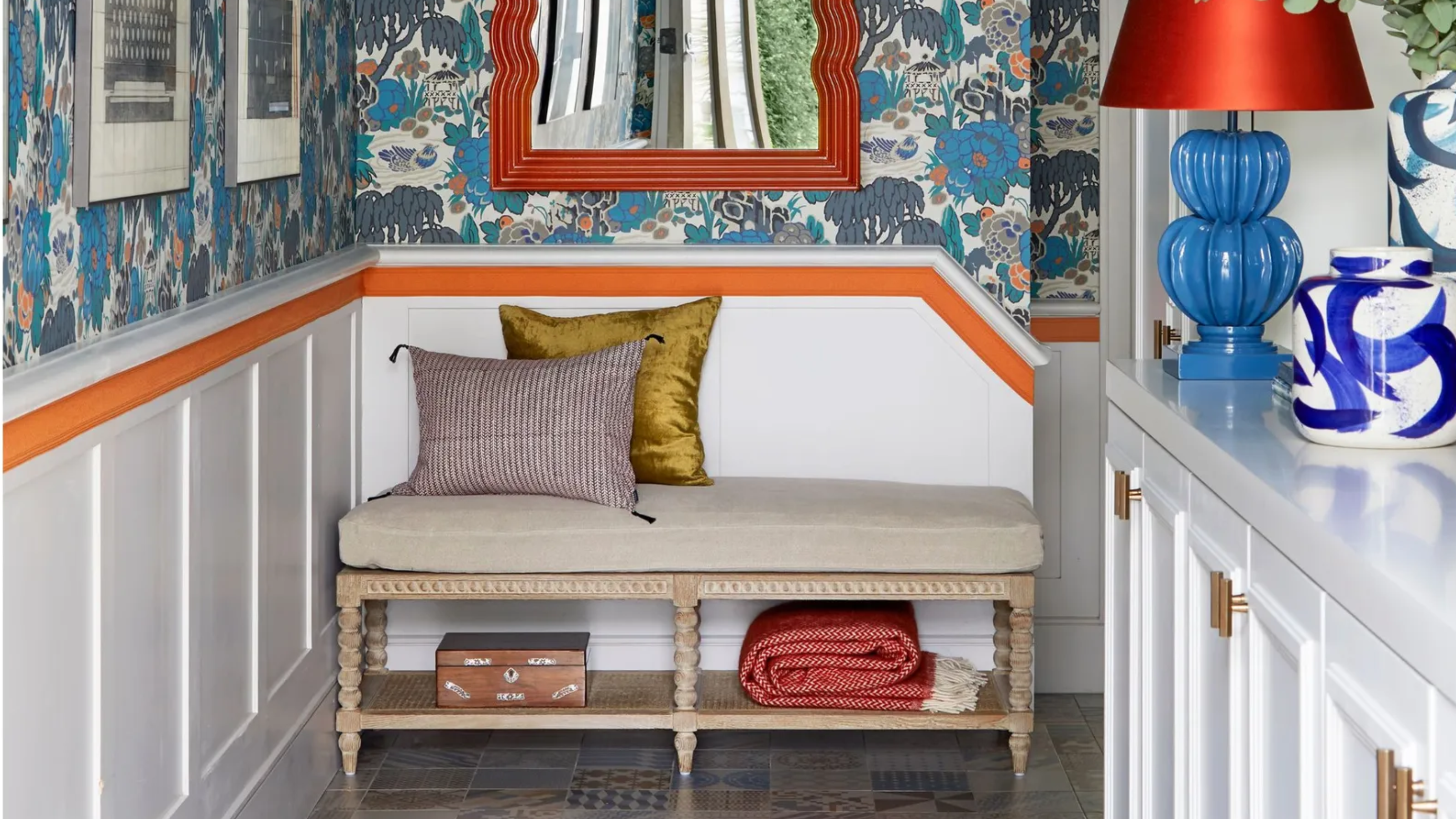 entryway with bold blue wallpaper and orange mirror and wall stripe