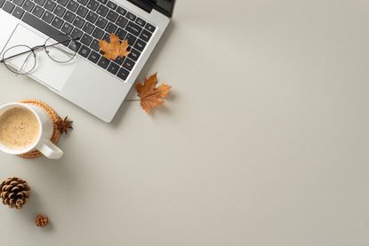 laptop on desk next to latte with fall leaves and pair of glasses
