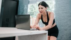 Woman in black sportwear types on laptop on kitchen counter