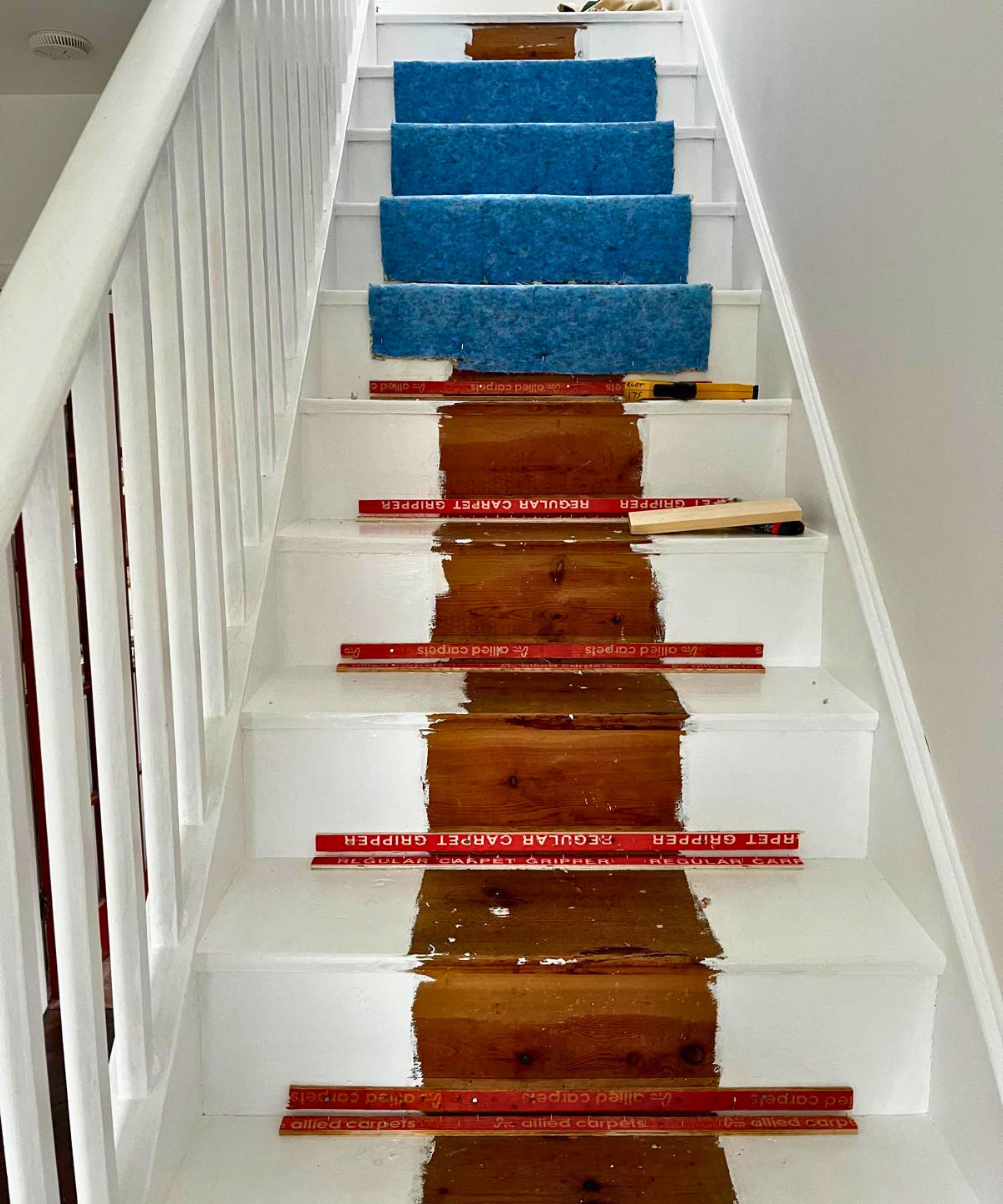 A mid-renovation staircase showing the treads being varnished with blue underlay still on upper steps.