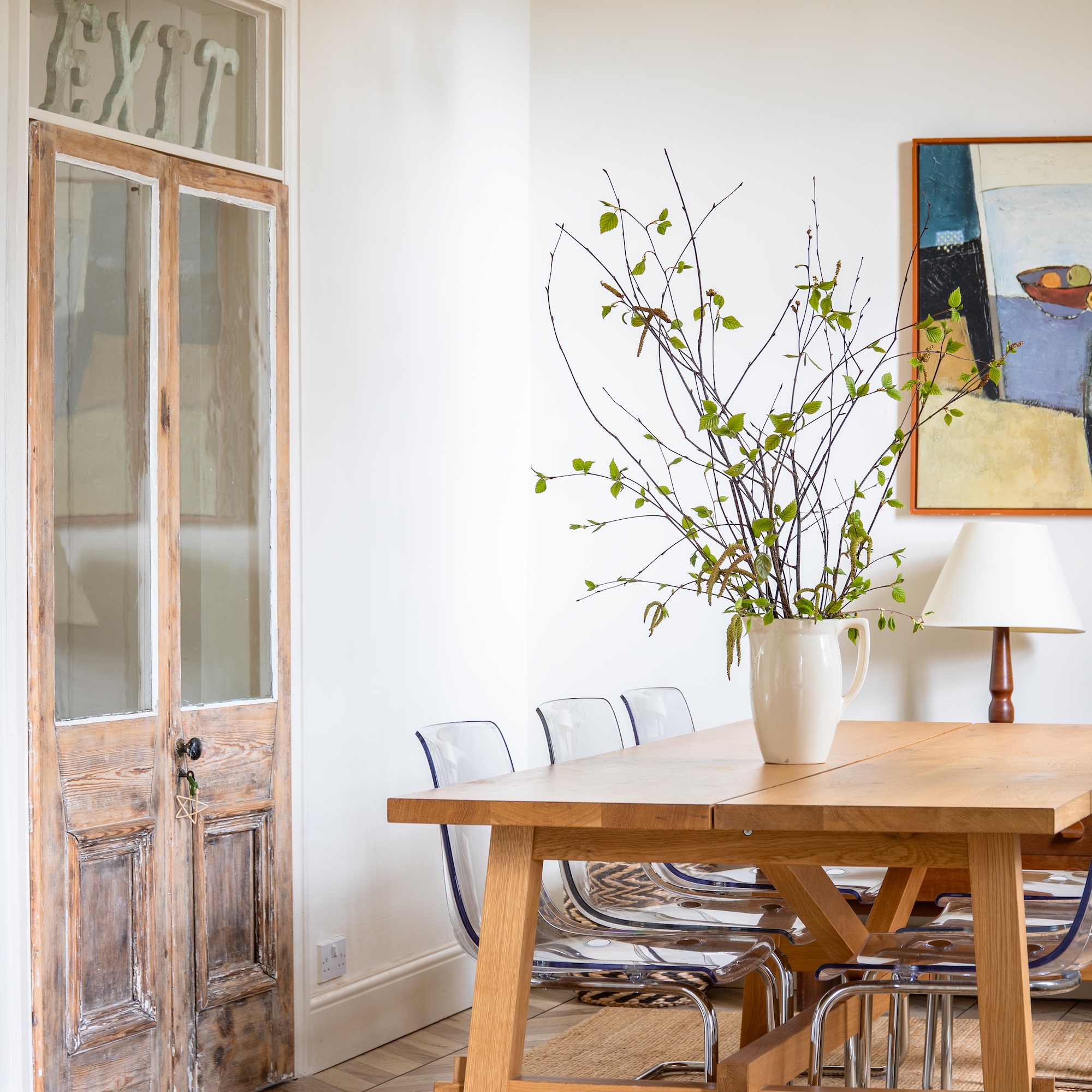 dining room with wooden table, clear plastic chairs and white jug with branches on table