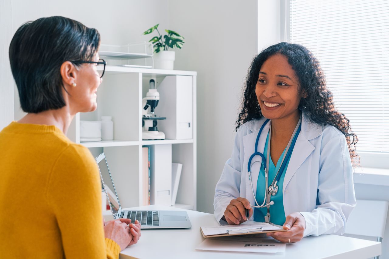 African-American doctor putting down patient medical complaints on clipboard in clinic office. Cheerful healthcare worker in lab coat and blue stethoscope. Concept of list of insurance business