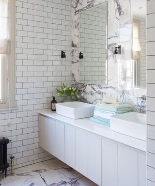 A white tiled bathroom with a long vanity unit in front of a marble wall