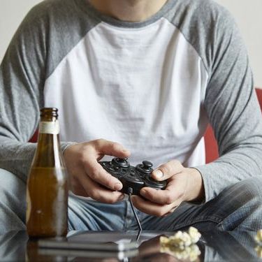 man playing a video game from a couch with a beer bottle on a table