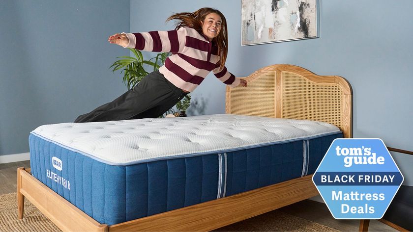 Our mattress tester jumping on the Bear Elite Hybrid mattress on a wooden bedframe with a rattan headboard in our sleep studio with blue walls and a bedside plant